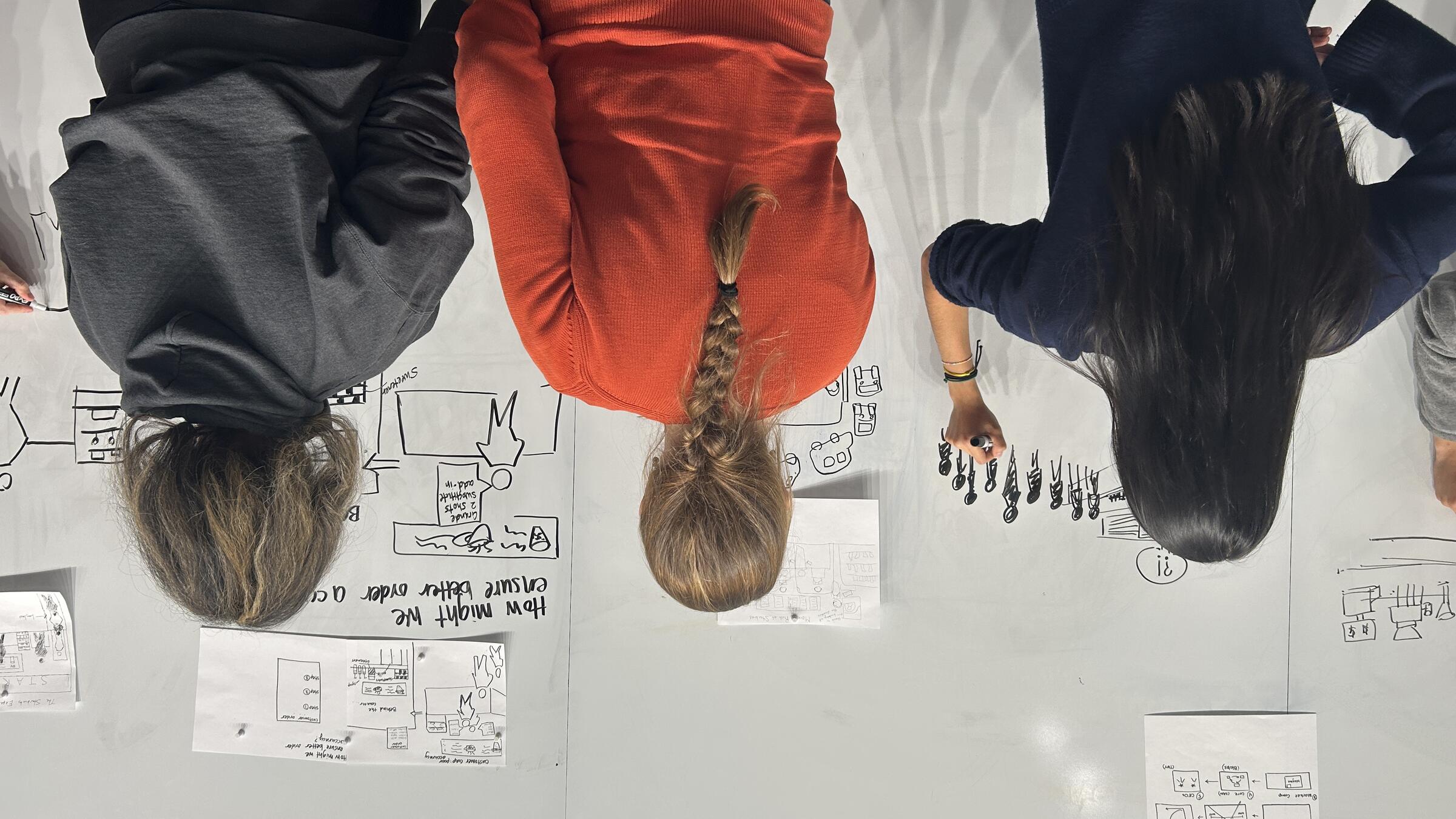 students stand at the whiteboard drawing diagrams