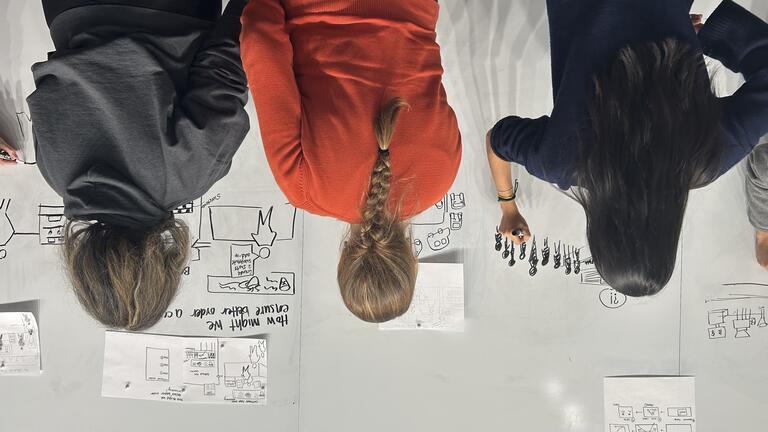 students stand at the whiteboard drawing diagrams