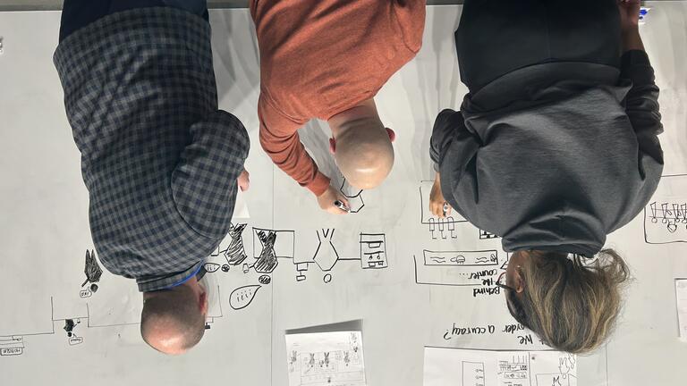 students stand at the whiteboard drawing diagrams together