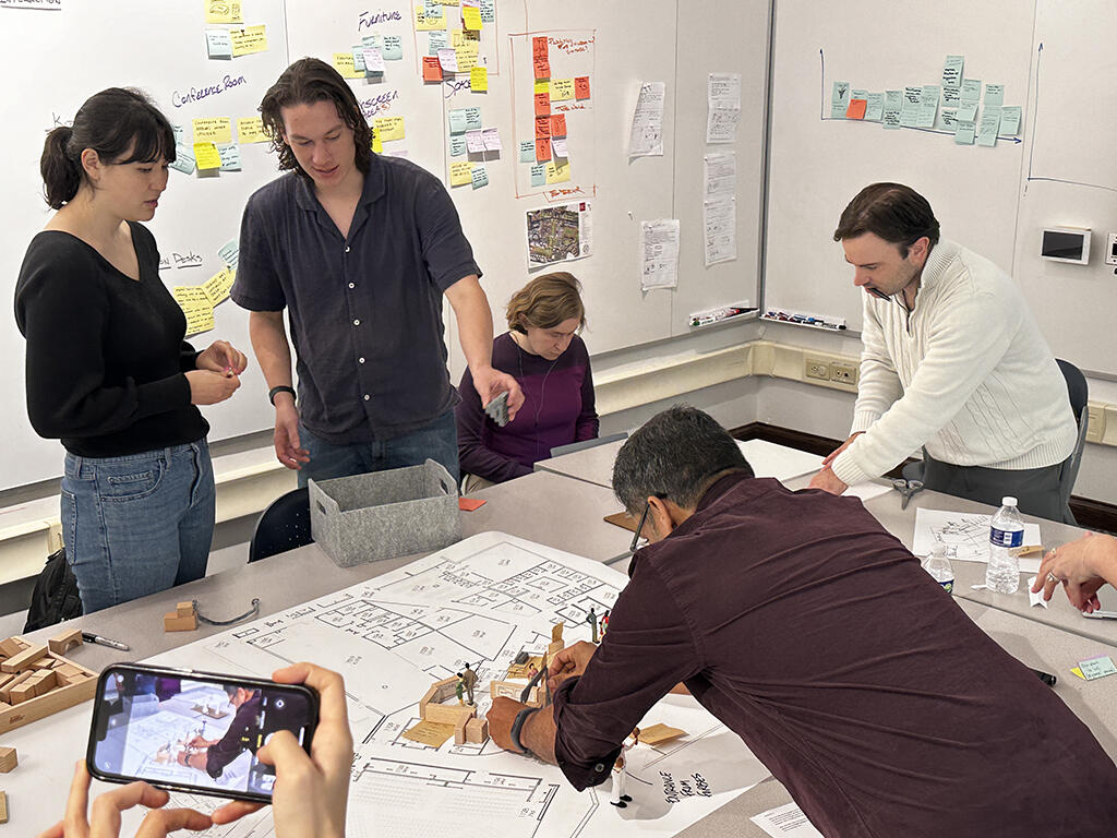 People working around a table-top space planning model and floor plan.
