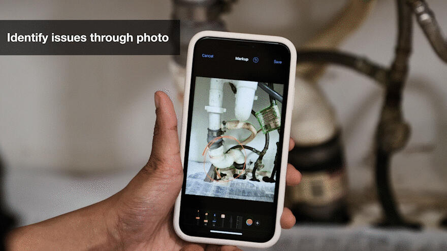 A smart phone taking a picture of a pipe under a sink